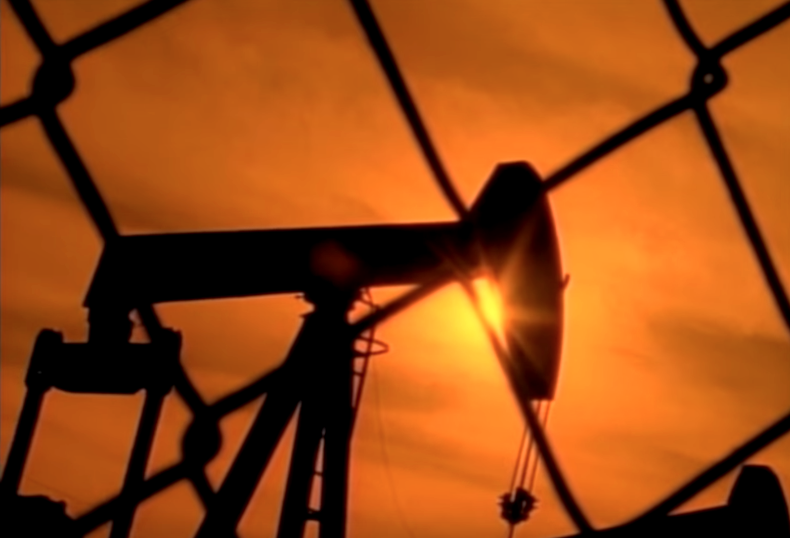 Oil rig pump, viewed through a chain length fence.