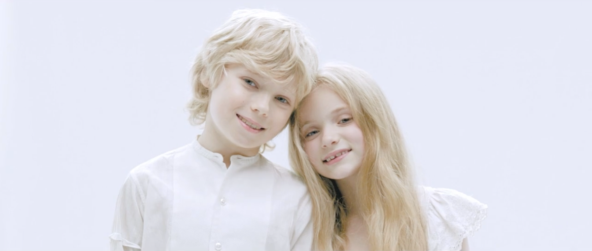 Two cute blonde kids smiling at the camera with white background.